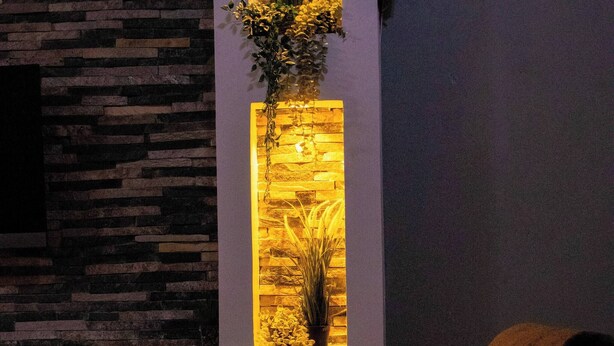 Een moderne woonkamer met een stenen muur, een verticale lichtinstallatie en een bank met kussens.