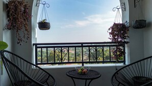 Een balkon met twee stoelen, een klein tafeltje met fruit, en hangende plantenbakken met gedroogde bloemen en groene planten.