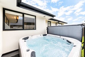 A hot tub in a backyard with a house in the background. - Spacious 4BR Home | Spa and Two Lounges + Games (Christchurch)