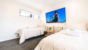 Ein Hotelzimmer mit zwei Betten, einem an der Wand befestigten Fernseher, einem kleinen Holzregal und einem Fenster.