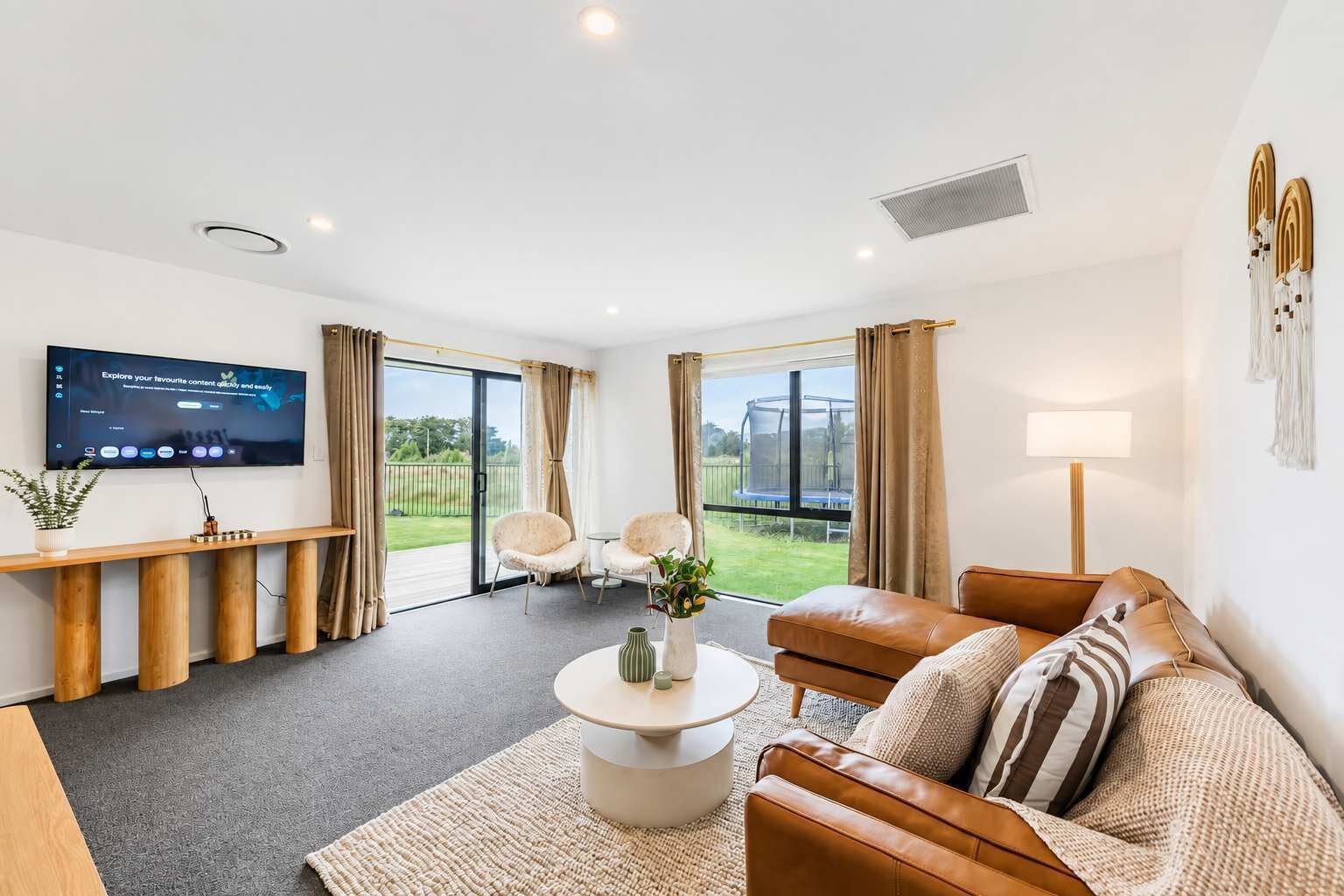 A modern living room with a flat-screen TV, leather sofa, and a view of the outdoors.