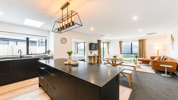 Eine moderne Küche mit Kochinsel, ein Essbereich mit Glastisch und ein Wohnzimmer mit Sofa und Fernseher.