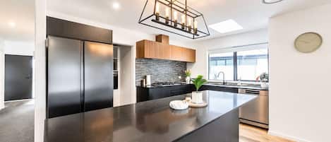A modern kitchen with a large island, stainless steel appliances, and a skylight.