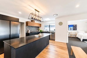 A modern kitchen with a central island, built-in appliances, and a contemporary light fixture. - Spacious 4BR Home | Spa and Two Lounges + Games (Christchurch)
