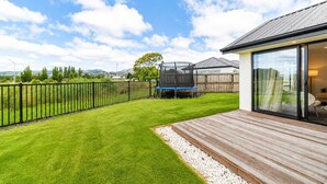 Ein gepflegter Garten mit einer Holzterrasse, einem Trampolin und freiem Blick auf die umliegende Landschaft.
