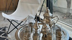 Una habitación moderna con una silla blanca, un ventanal grande y una bandeja con vasos y una tetera.
