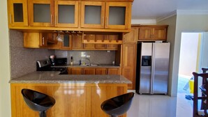 Une cuisine avec des meubles de rangement en bois, un réfrigérateur en acier inoxydable et deux tabourets de bar.