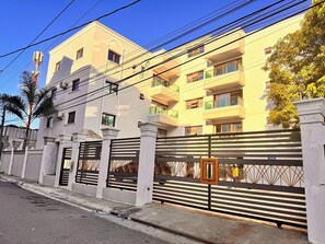 A multi-story residential building with a gated entrance, a palm tree, and a clear blue sky. - Enjoy Huge 4 bedrooms, and 3 bathrooms, 8 new apartments (Santiago de los Caballeros)