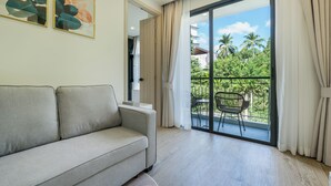 En moderne stue med sofa, balkon med bord og stole samt udsigt til grønt og bygninger.