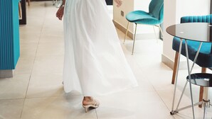 En kvinde i en hvid kjole går gennem en moderne hotellobby med turkise stole og en glasvæg.
