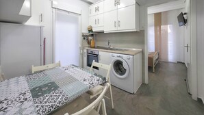 Ett kompakt kök med tvättmaskin, ett matbord med ett mönstrat bordsduks och en liten ugn.