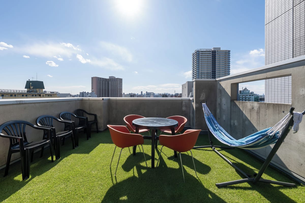 A rooftop terrace with a round table and chairs, a hammock, and a view of city buildings.