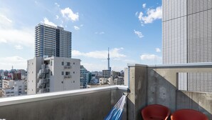 Un balcón con una hamaca, dos sillas rojas y vistas a un paisaje urbano que incluye un edificio alto y una torre.