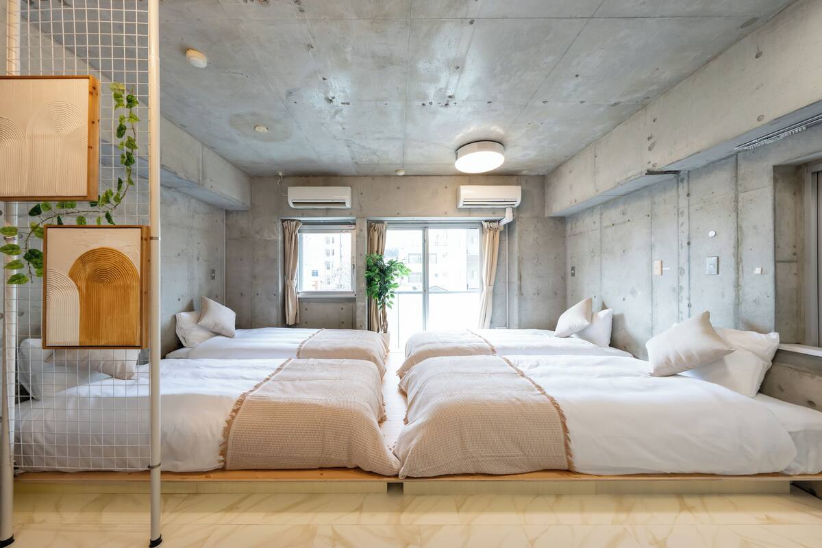 A modern hotel room with two beds, a wooden headboard, air conditioning units, and a large window with curtains.