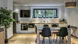 A modern kitchen with a central island, white cabinetry, and a large window providing natural light. - Gorgeous home in Noves (Noves)