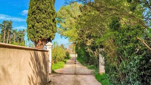 A gated driveway leading to a building with a concrete wall on one side and a metal gate. - Gorgeous home in Noves (Noves)