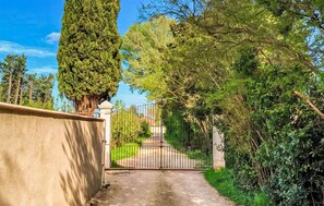 A gated driveway leading to a building with a concrete wall on one side and a metal gate. - Gorgeous home in Noves (Noves)