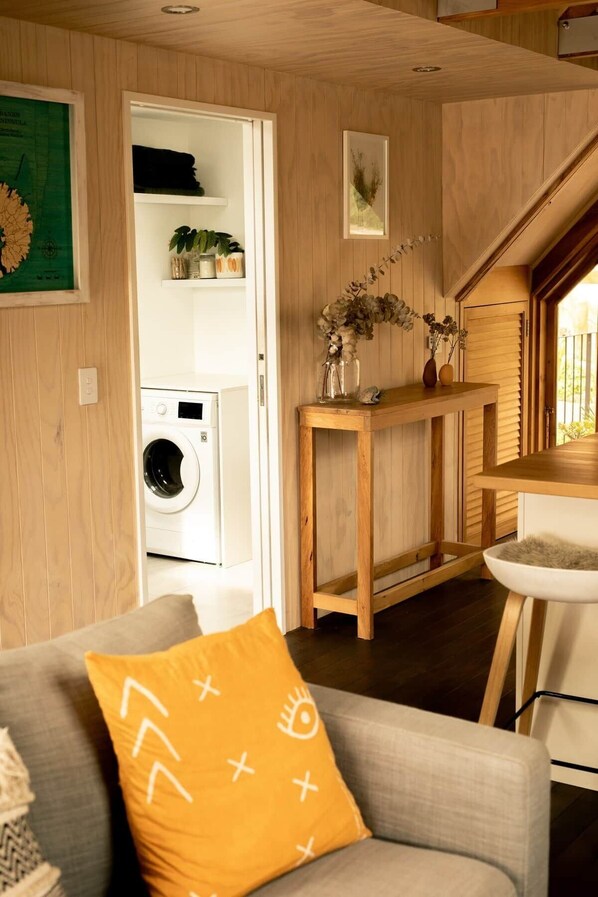 A cozy living area with a sofa, a wooden table, a washing machine, and a staircase leading to another level.