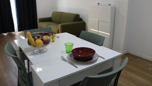 A dining area with a white table, green chairs, a red bowl, a fruit bowl, and a green glass. - Flamingo Houses (Quartu Sant'Elena)