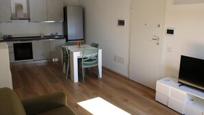 A compact living space with a kitchenette, dining area, and a TV on a stand. - Flamingo Houses (Quartu Sant'Elena)