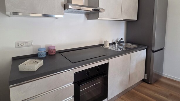 A modern kitchen with a built-in oven, a stainless steel refrigerator, and a black countertop. - Flamingo Houses (Quartu Sant'Elena)