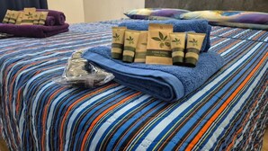 A bed with a striped blue and orange bedspread, a purple towel, and several toiletries including a tube of lotion and a bar of soap. - Flamingo Houses (Quartu Sant'Elena)