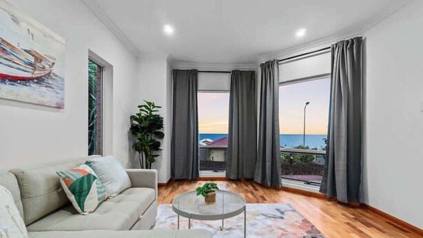 Un salon moderne avec un canapé, une table basse et une vue sur la mer grâce à de grandes fenêtres.