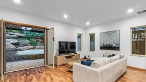Un salon moderne avec un canapé, un téléviseur et une porte vitrée donnant sur un jardin.