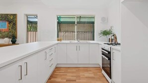 Une cuisine moderne avec des meubles blancs, un plancher en bois, un évier, une cuisinière et une fenêtre donnant sur un paysage verdoyant.