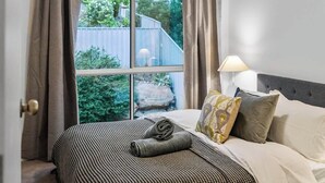 Une chambre avec une grande fenêtre, un lit avec une literie à rayures et une lampe sur une table de chevet.