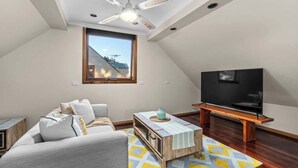 Un salon moderne avec un ventilateur de plafond, une grande fenêtre, un canapé, une table basse et un téléviseur.