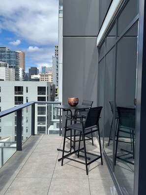A modern balcony with a table and chairs, large windows, and a city view. - City view focused comfy apartment free parking (Adelaide)