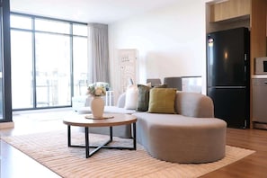 A modern living room with a sofa, coffee table, and a black refrigerator. - City view focused comfy apartment free parking (Adelaide)