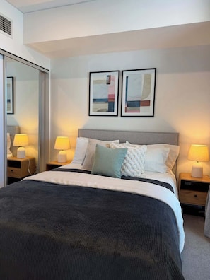 A modern bedroom with a large bed, two bedside tables with lamps, a wardrobe, and abstract artwork on the wall. - City view focused comfy apartment free parking (Adelaide)