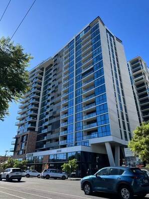 A multi-story building with a modern architectural design, featuring a prominent entrance with a sign, and several cars parked in front. - City view focused comfy apartment free parking (Adelaide)