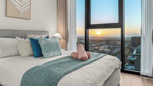 A hotel room with a large bed, a view of the city, and a framed leaf artwork on the wall. - City sky view self service apartment free parking (Adelaide)