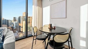 A modern room with a large window, a round dining table, and a sofa. - City sky view self service apartment free parking (Adelaide)