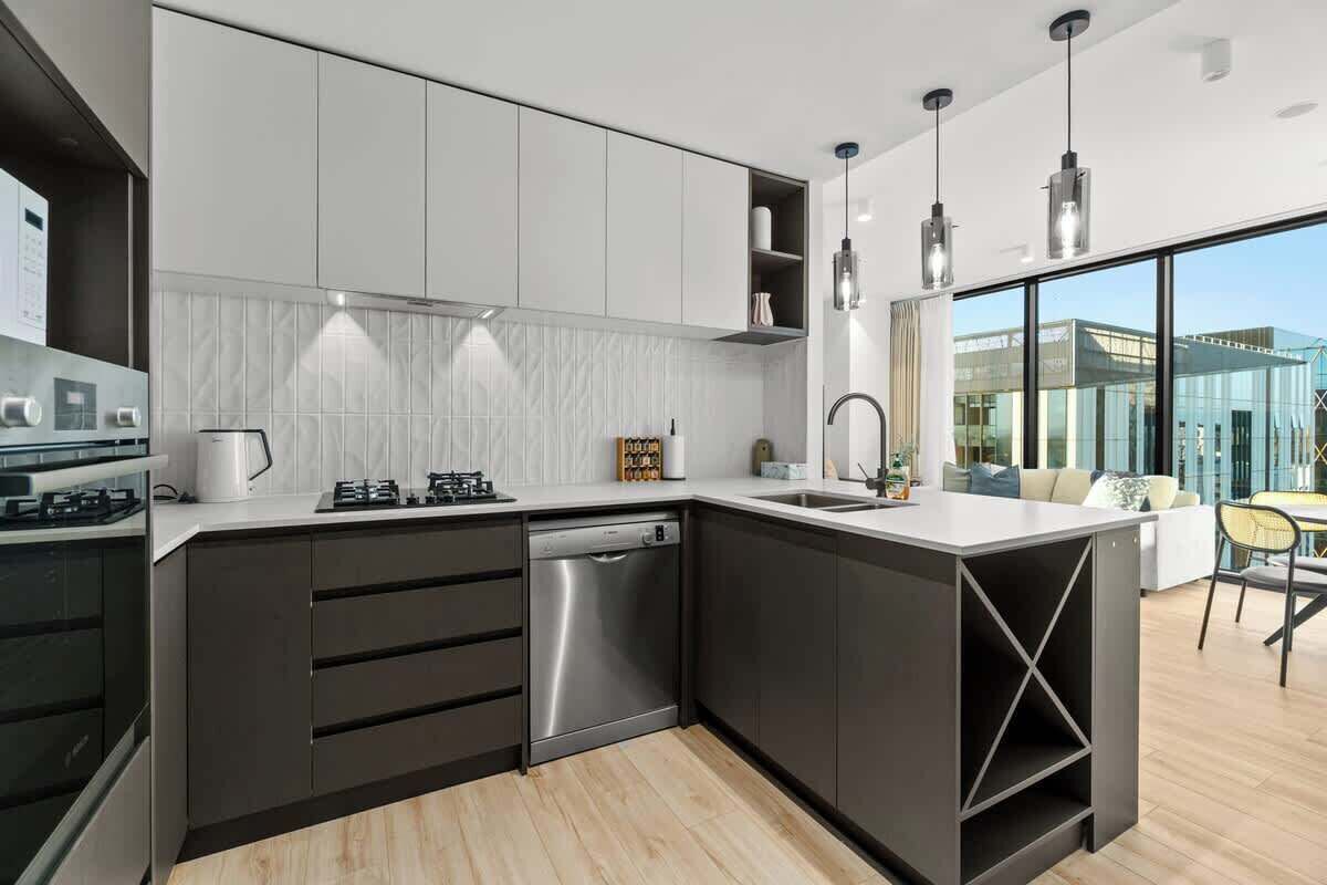 A modern kitchen with dark cabinetry, a dishwasher, and a built-in oven.