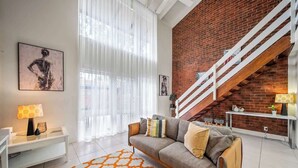 A modern living room with a brick wall, a staircase, a sofa, a coffee table, and a rug. - Urban Sanctuary Condo in Norwood 2b1b+free parking (Norwood)