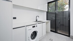 A compact laundry room with a washing machine, a sink, and a sliding glass door leading to a backyard. - Large Family entire house adelaide 4br2ba (Rostrevor)
