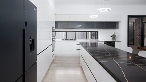A modern kitchen with white cabinetry, a black refrigerator, and a black countertop with a marble-like pattern. - Large Family entire house adelaide 4br2ba (Rostrevor)