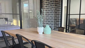 A modern dining area with a long wooden table, black chairs, and a brick wall. - Large Family entire house adelaide 4br2ba (Rostrevor)