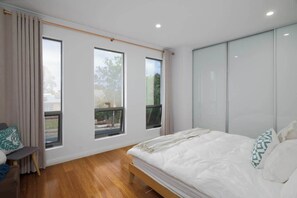 Een slaapkamer met een bed, een stoel, een bureau en grote ramen.