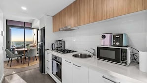 A modern kitchen with white cabinets, a gas stove, a sink, and a microwave. - Comfort city view apartment Central Adelaide (Adelaide)