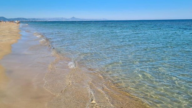 Een strand met helder ondiep water en een bergketen in de verte.