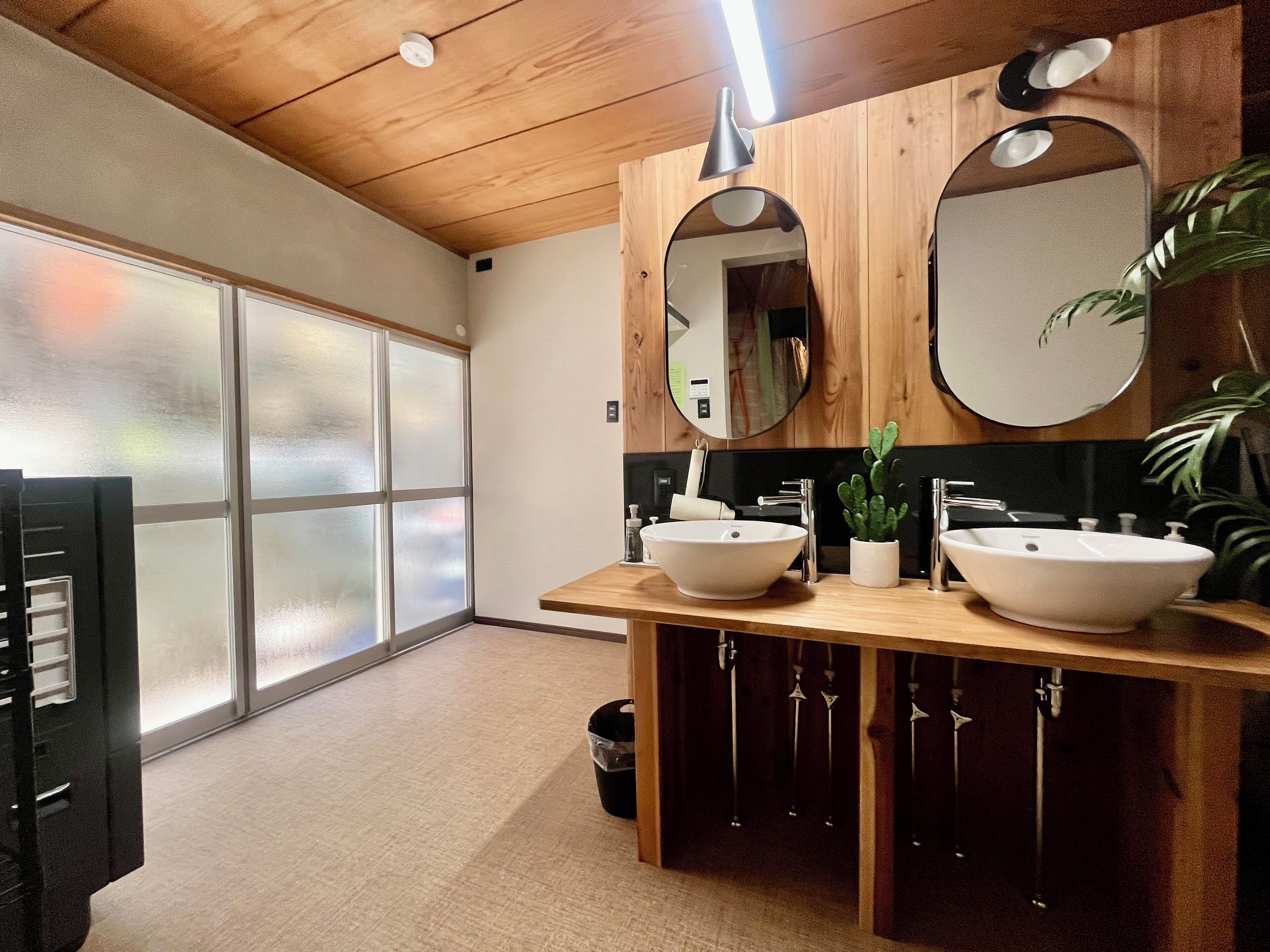 A modern bathroom with two sinks, wooden vanity, mirrors, and a potted plant.