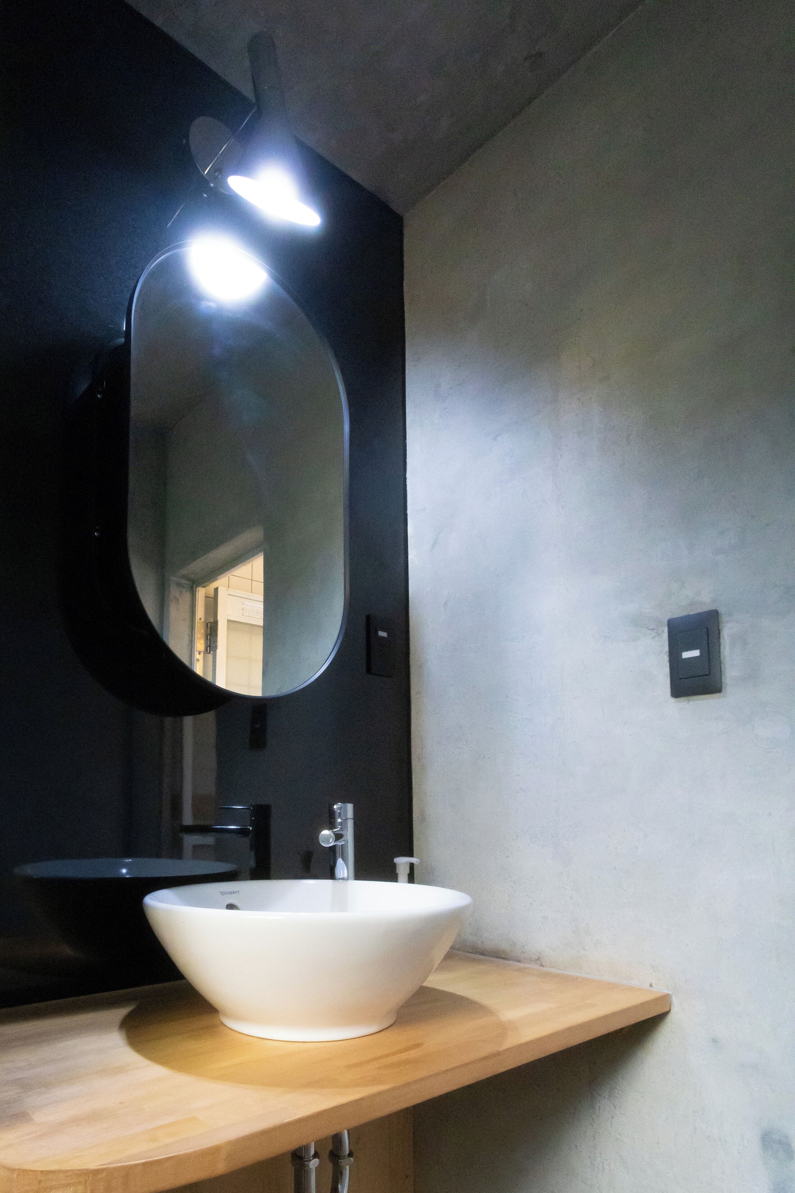 A bathroom with a white sink, a black mirror, and a wooden countertop.