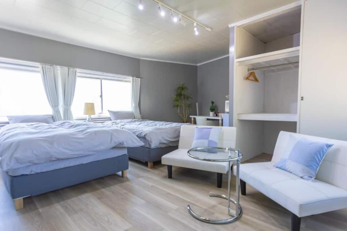 A modern bedroom with two beds, a white sofa, a small table, and a walk-in closet.