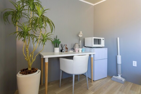 A small, modern kitchen with a white countertop, a microwave, a coffee maker, and a potted plant.