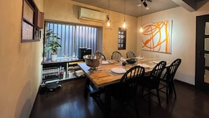 A dining area with a wooden table, black chairs, hanging pendant lights, a large abstract painting, and a potted plant. - HABi-Wakaura (Wakayama)